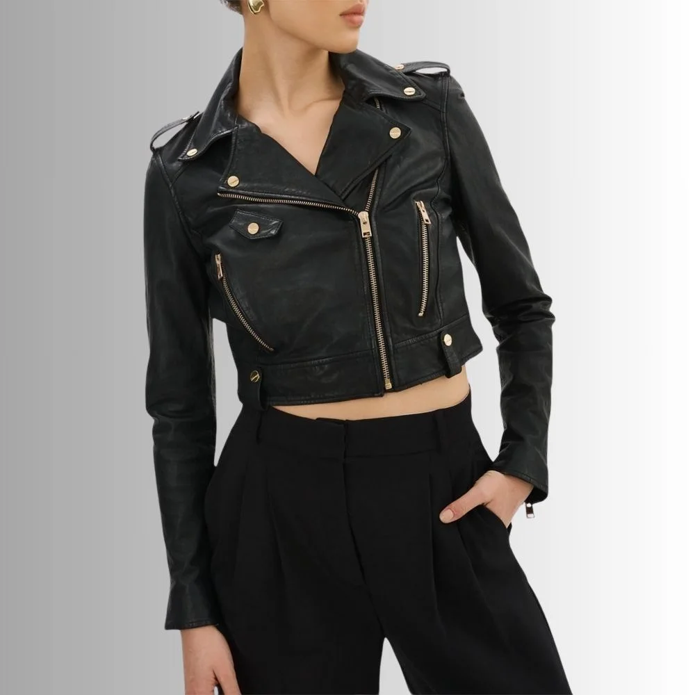 Woman in a black cropped leather biker jacket, showing its gold zippered pockets and bold lapel design.