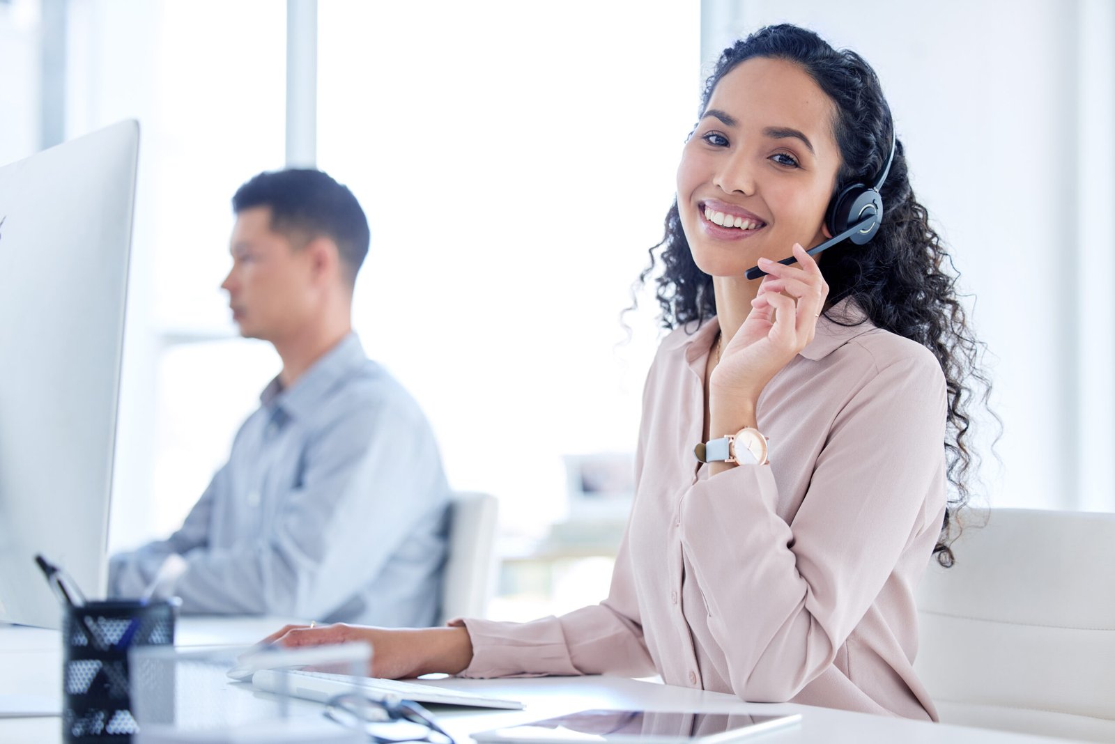 A smiling female customer service representative wearing a headset in a bright office.